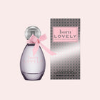 A bottle of Born Lovely Eau de Toilette perfume next to its retail box, set against a solid pale pink background. The bottle is a translucent lavender-purple color with a silver faceted cap and a pink satin bow, while the box features a silver and black honeycomb pattern with a pink label.