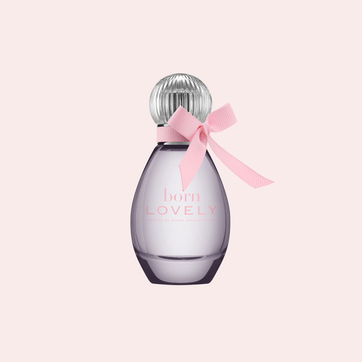 A bottle of Born Lovely Eau de Parfum by Chanel, featuring a translucent lavender-purple glass bottle, a silver ribbed cap, and a light pink satin ribbon tied in a bow around the neck, set against a solid pale pink background.
